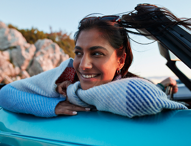 person leaning on car with hands folded under chin